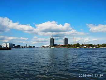 Buildings by river against cloudy sky