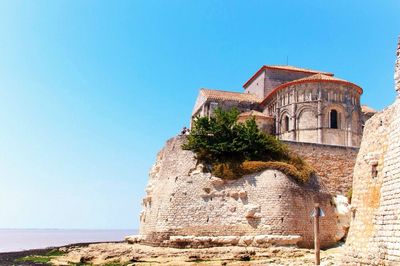 Low angle view of church by sea against clear blue sky on sunny day