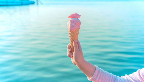 Cropped hand of girl holding ice cream cone against sea