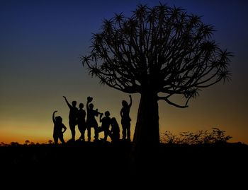 Silhouette people standing by tree on field against sky during sunset