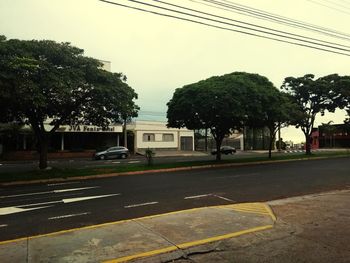 Road by trees against sky in city