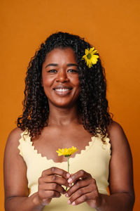 Portrait of young woman holding gift against yellow background