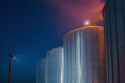 Low angle view of illuminated factory against sky at dusk