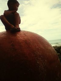Man sitting on beach against sky