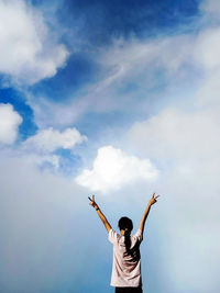 Rear view of man with arms outstretched standing against sky