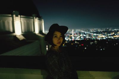 Portrait of woman standing against illuminated cityscape at night