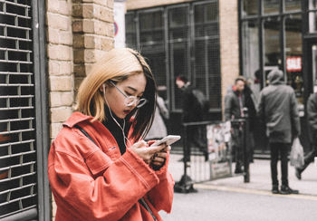 Young woman using smart phone while standing on street in city