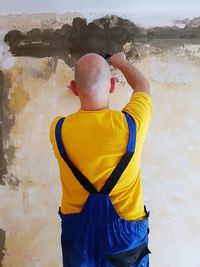 Rear view of a boy standing against wall