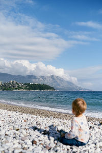 Rear view of boy on pebbles at beach against sky