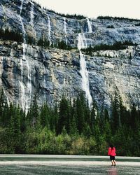 Rear view of woman standing by waterfall against mountain