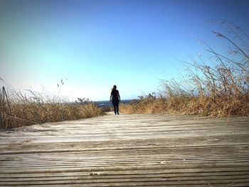 Rear view of man walking on street against clear sky