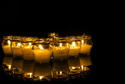 Illuminated tea light candles on table with reflection in darkroom