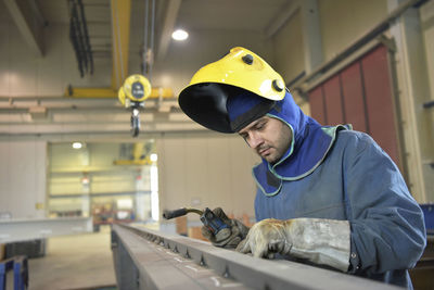 Welder checking metal surface in factory