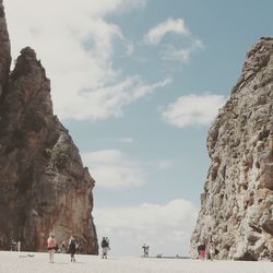 People by rock formations at sandy beach against sky