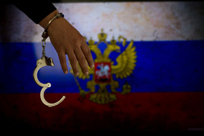 Cropped hand of male criminal with handcuffs against russian flag