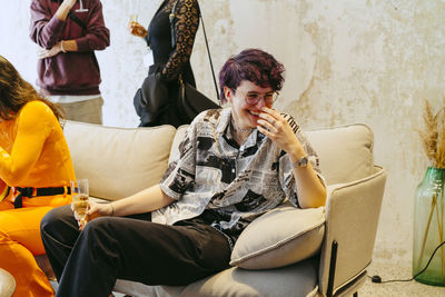 Happy non-binary person laughing while sitting on sofa during event at convention center