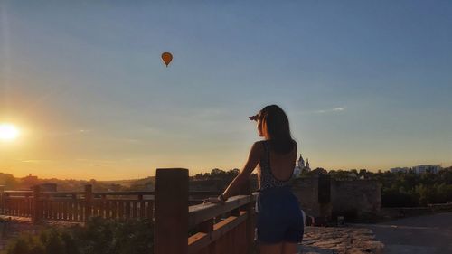 Woman standing by cityscape against sky during sunset