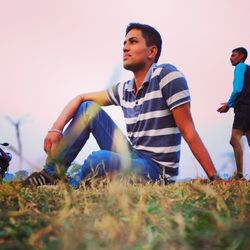 Young man looking away on field against clear sky