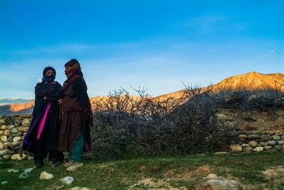 Rear view of man and woman standing against sky during sunset