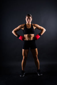 Portrait of young woman exercising against black background