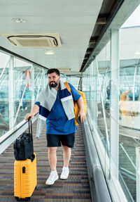 Man with yellow suitcase and backpack boarding plane walking through glass boarding corridor airport