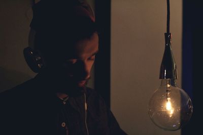 Mid adult man listening music on headphones by illuminated light bulb in dark
