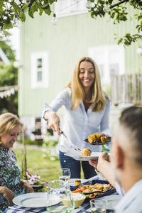 Female serving grilled corns to friends at dining table in backyard party