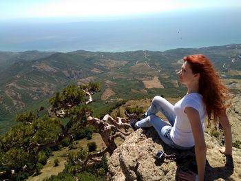 Woman sitting on cliff against sky