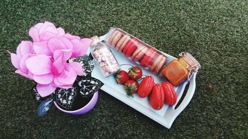 High angle view of artificial pink flowers by macaroons and strawberries on field