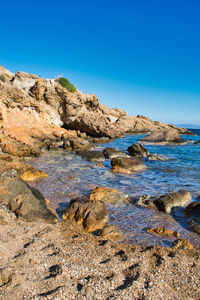 Rocks in sea against clear blue sky