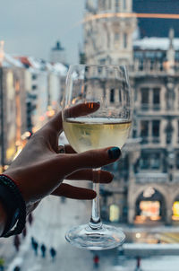 Close-up of hand holding wineglass against city