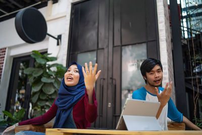 Low angle view of couple with digital tablet on table gesturing while sitting at sidewalk cafe