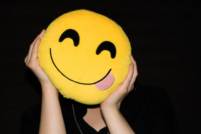 Close-up portrait of woman holding yellow paper against black background