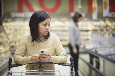 Woman doing shopping in supermarket and holding cell phone