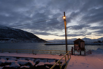 Illuminated light on jetty in fjord against cloudy sky at dawn