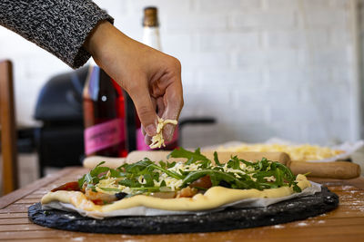 Hand throwing cheese into a vegetarian pizza.