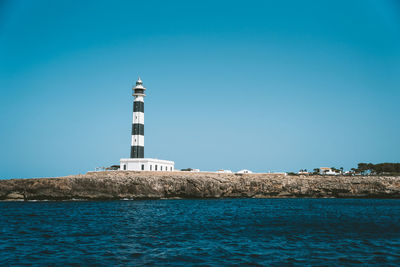 Lighthouse by sea against clear blue sky