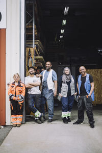 Full length of smiling male and female colleagues standing outside warehouse