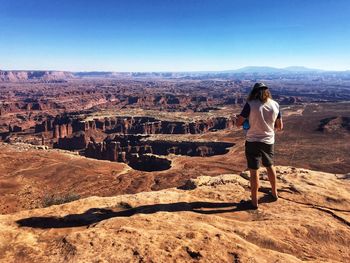 Rear view of woman standing on rock against clear sky