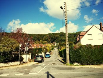 Cars on road by trees against sky in city