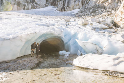 Retired couple emerge from glacial ice cave during luxury tour.