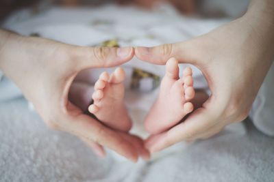 Mother making heart shape around baby feet at home