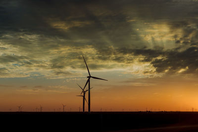 Silhouette wind turbines on field against sky during sunset