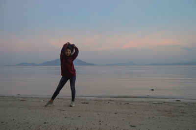 Rear view of woman standing at beach against sky during sunset