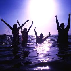 Silhouette people enjoying in sea against sky during sunset