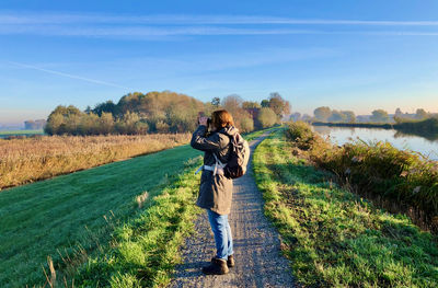 A woman stands on a rural dike and watches the landscape through binoculars