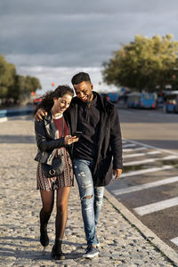 Smiling couple looking at phone while walking outdoors