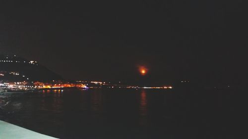 Illuminated city by sea against clear sky at night