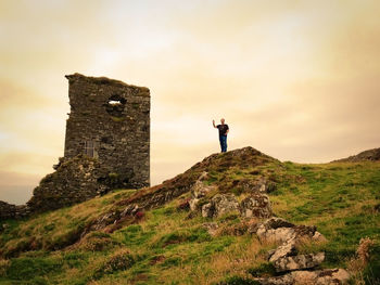 Low angle view of man standing on rock formation by old ruins against sky