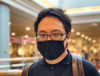 Close-up portrait of young man in face mask and eyeglasses against neon lights inside mall.